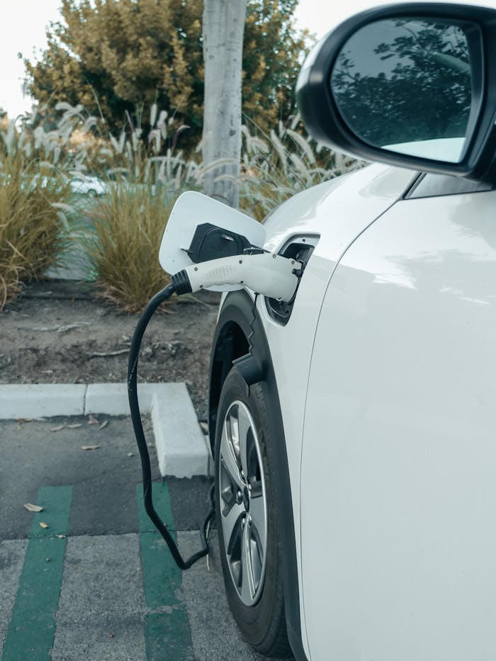 A white electric car plugged into a charger at an outdoor parking area, promoting clean energy.